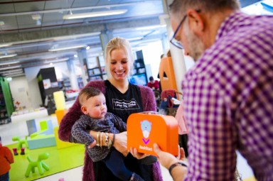 Een moeder en baby krijgen van een man een BoekStartkoffertje uitgereikt, in de plaatselijke bibliotheek